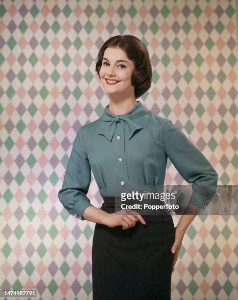 Posed studio portrait of a female fashion model wearing a blue autumnal fitted blouse with bow collar, London, 11th October 1958.
