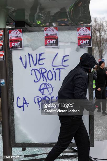 Black bloc passant devant un panneau d'affichage lumineux d'un abribus vandalisé avec une inscription anarchiste "Vive le droit de la paresse" et...