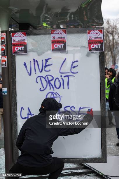 Black bloc écrivant sur un panneau d'affichage lumineux d'un abribus vandalisé l'inscription anarchiste "Vive le droit de la paresse" et autocollants...