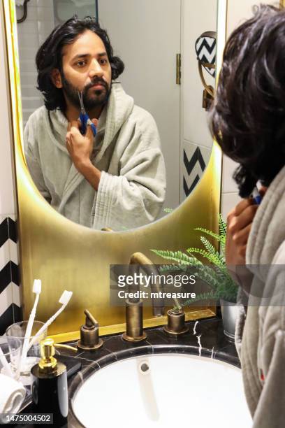 nahaufnahme der reflexion im spiegel eines indischen mannes, der im bademantel mit einer schere im badezimmer stand, bart und schnurrbart schneiden, künstliche farnpflanze im metalltopf, zahnbürsten aus glas, selbstpflege- und pflegekonzept - bathroom pot plant stock-fotos und bilder