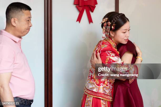 a beautiful chinese bride hugs her mother while her father watches from behind - chinese traditional dress stock pictures, royalty-free photos & images