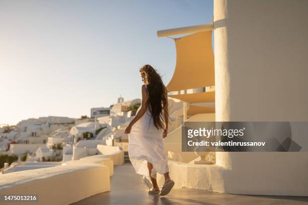 joven mujer asiática con vestido blanco en unas vacaciones en santorini, disfrutando de la vista de la arquitectura tradicional - greece city fotografías e imágenes de stock