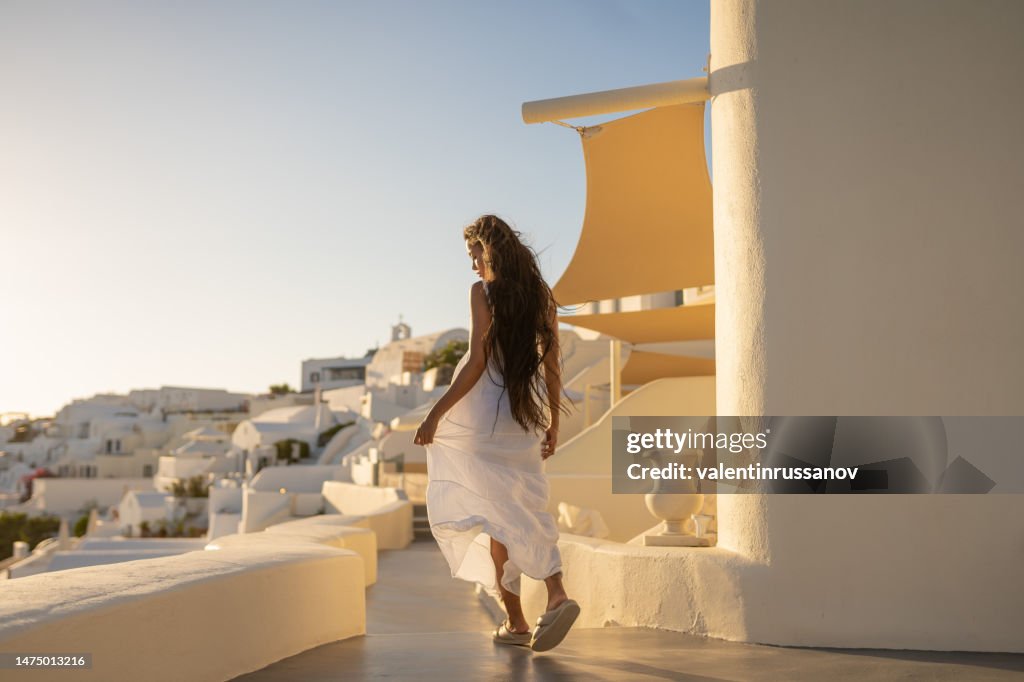 Young female asian woman with white dress on a vacation in Santorini, enjoying the view of the traditional architecture