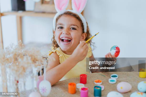 child girl painting easter eggs looking at camera - easter and humour stockfoto's en -beelden