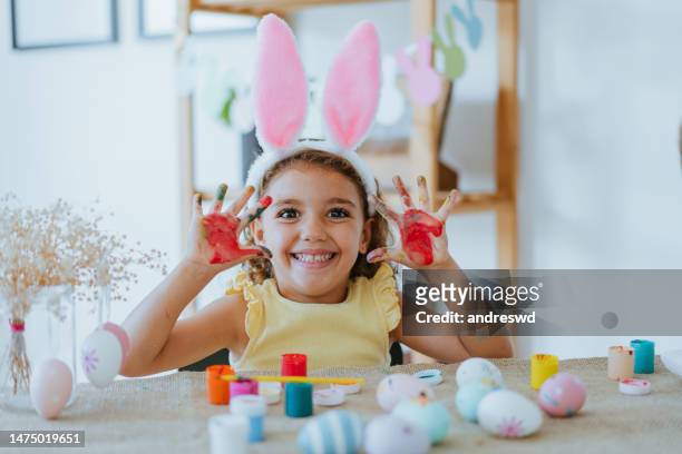 child girl painting easter eggs looking at camera - dirty easter stock pictures, royalty-free photos & images