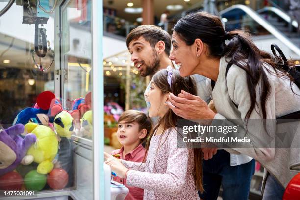 little girl playing with toy grabbing machine while surrounded by family - claw machine stock pictures, royalty-free photos & images