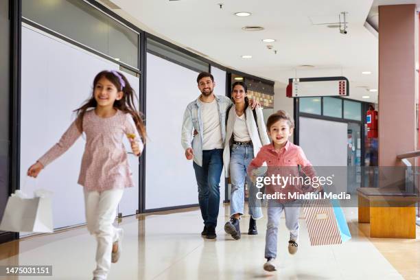 young adult couple walking while children are running on mall's hallway - family mall stockfoto's en -beelden