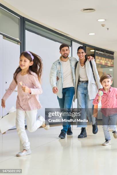 young adult couple walking while children are running on mall's hallway - latin american and hispanic shopping bags stock pictures, royalty-free photos & images