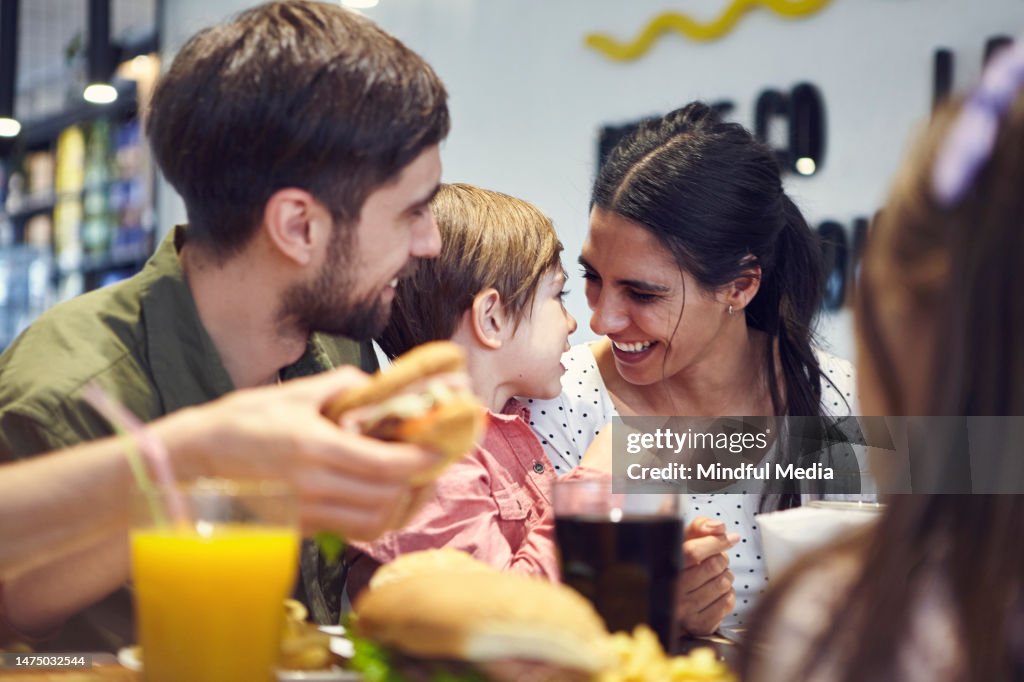 Glückliches Paar, das Hamburger mit kleinem Sohn im Food Court des Einkaufszentrums isst