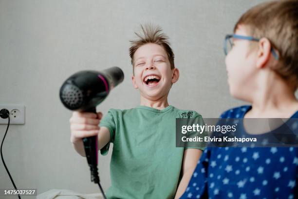 portrait of two boys in pajamas playing with a hair dryer and drying their hair - haardroger stockfoto's en -beelden