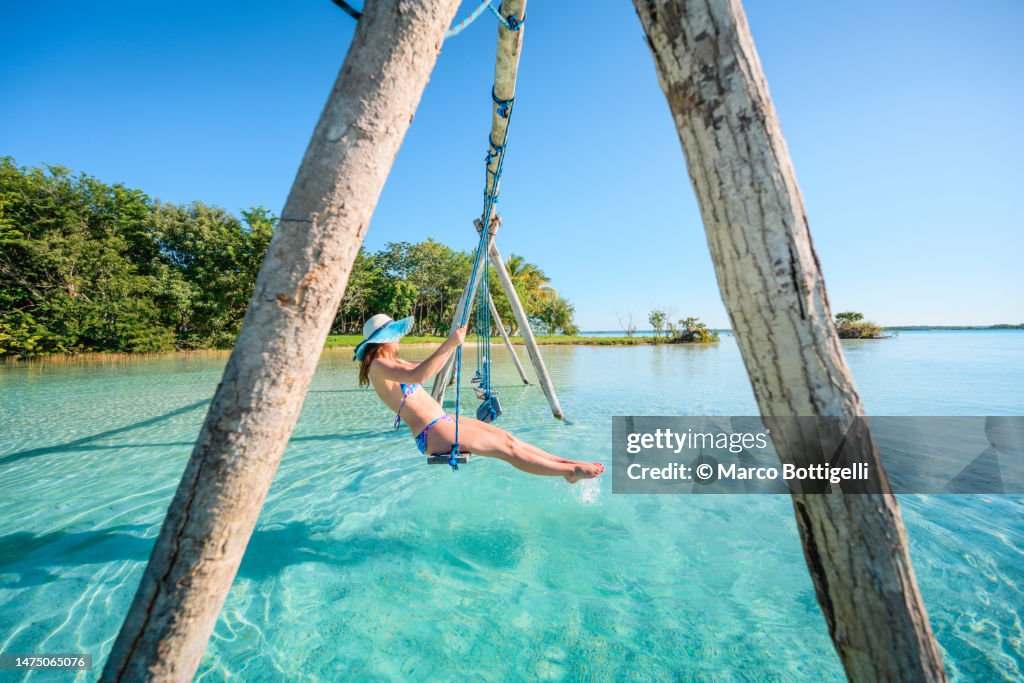 Woman playing on a swing over turquoise tropical water