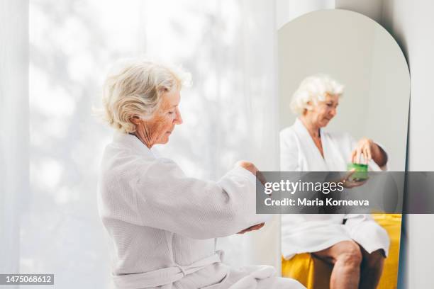 senior woman applying cream on hands in the morning. - trattamento di bellezza foto e immagini stock