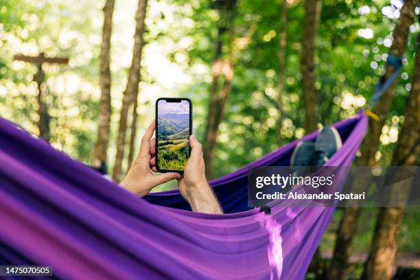 man using smartphone while relaxing in a hammock - taking photo with phone stock-fotos und bilder