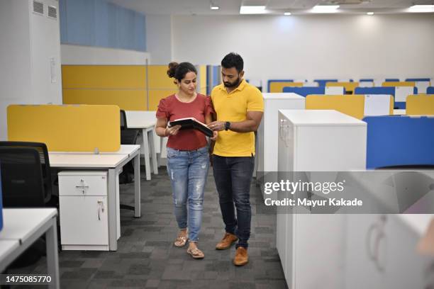 co-workers discussing while walking in an office corridor carrying documents in hands - india partition stock pictures, royalty-free photos & images