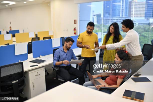 co-workers gathered in an office cubicle working and discussing using laptop and documents - india office stock pictures, royalty-free photos & images
