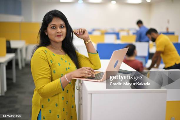 mature woman looking at the camera  while working on a laptop standing near her cubicle in an office - women india partition stock pictures, royalty-free photos & images