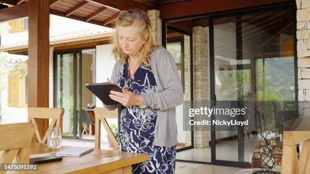 donna anziana attiva che utilizza la tavoletta digitale in piedi vicino al tavolo a casa - nl ebook foto e immagini stock