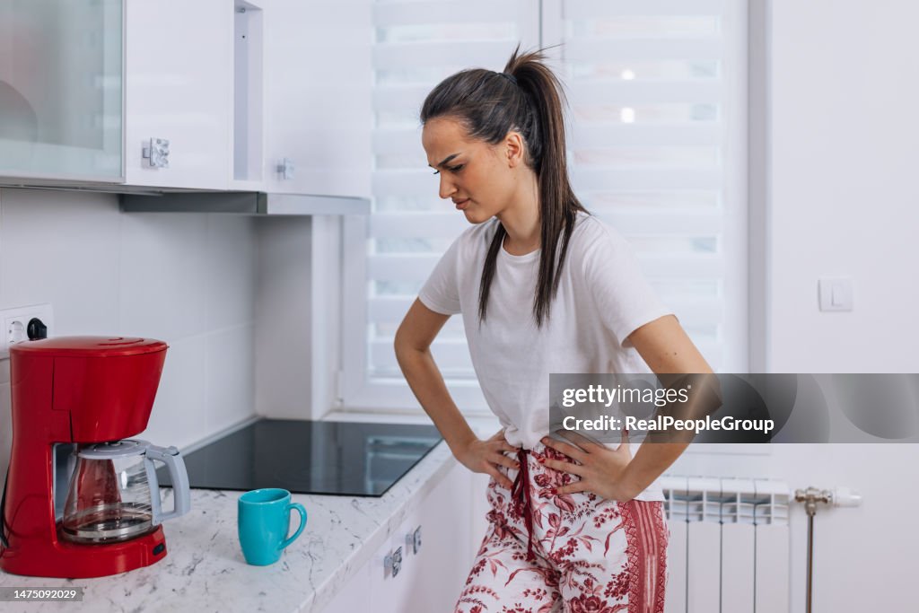 Young woman in kitchen holding her painful stomach
