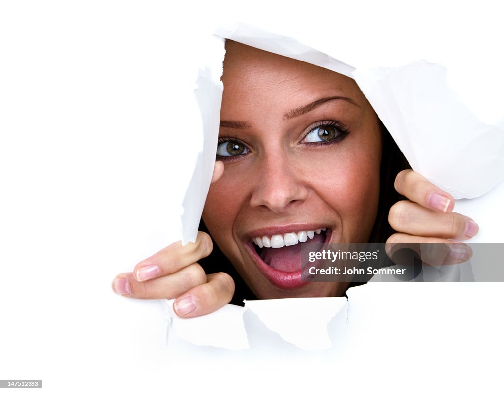 Happy young woman ripping through paper wall