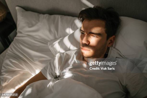 man lying in a bed and waking up - sleepless stock pictures, royalty-free photos & images