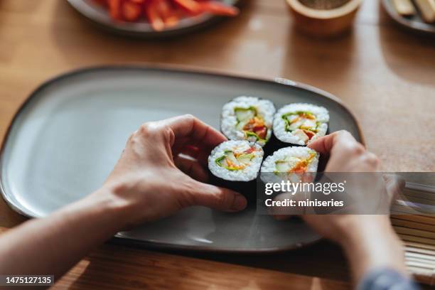 photo rapprochée de mains de femme servant des rouleaux de sushi sur une assiette - accompagnement professionnel photos et images de collection