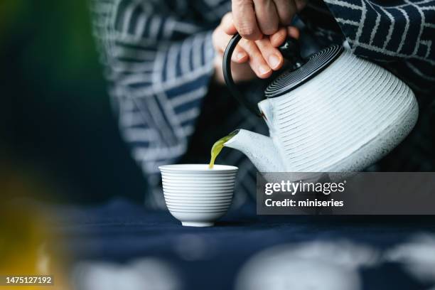 nahaufnahme von frauenhänden, die matcha-grüntee aus der teekanne in eine tasse gießen - matcha stock-fotos und bilder