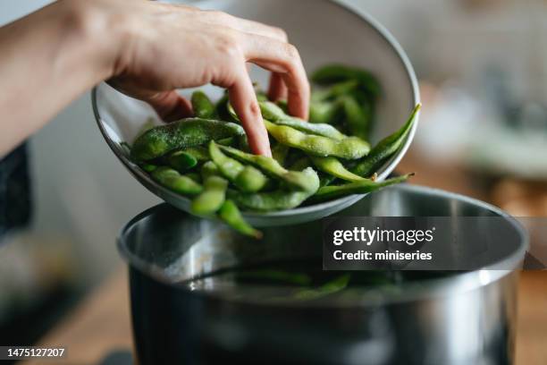 foto de primer plano de manos de mujer agregando edamame a la olla en la cocina - hervir fotografías e imágenes de stock