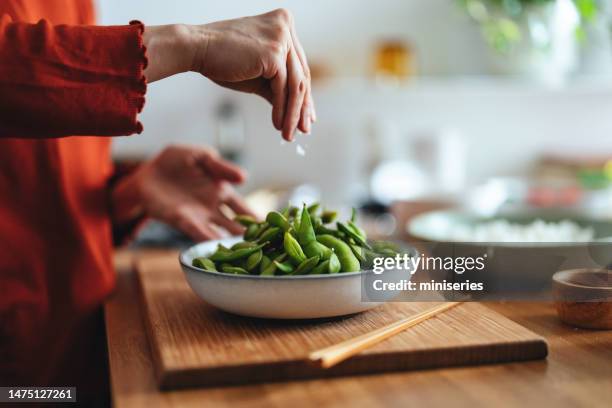 close up photo of woman hand salting cooked edamame beans at home - edamame stock pictures, royalty-free photos & images