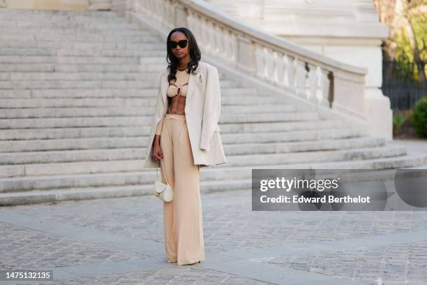 Emilie Joseph wears sunglasses, a golden necklace, a white bag from Cafune, a white oversize blazer jacket, a beige crop top with keyholes from from...