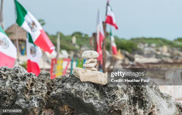 stacked rocks placed on a rocky ledge with mexican flags in the background - naturalist beach stock pictures, royalty-free photos & images