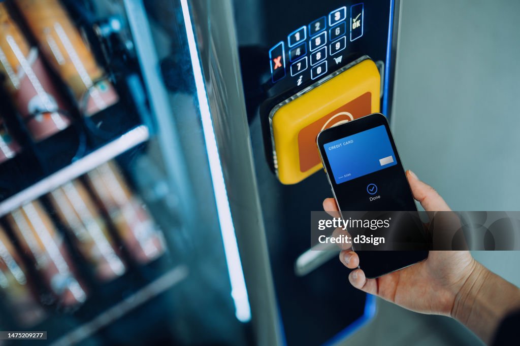 Close up of woman's hand paying for the product at vending machine with contactless payment, using digital wallet on smartphone. Credit card payment. E-commerce. Tap to pay