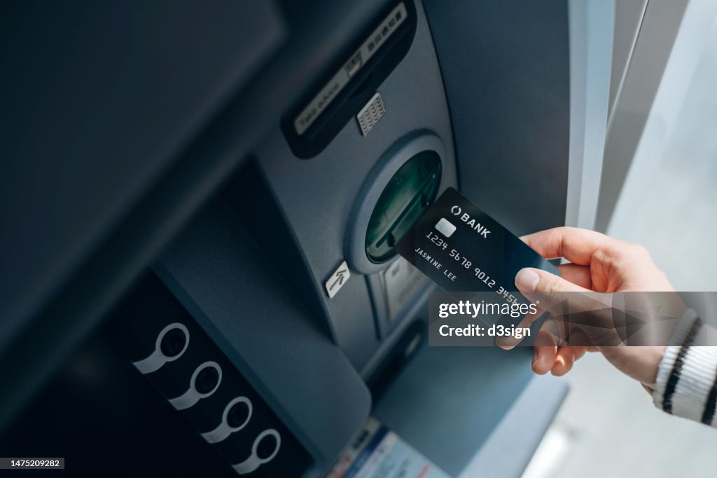 High angle shot of female hand inserting her bank card into automatic cash machine in the city. Withdrawing money, paying bills, checking account balances and make a bank transfer. Privacy protection, internet and mobile banking security concept