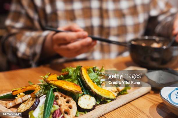 man eating with a plate of colorful grilled vegetables in front of him on the table - adult eating no face stock pictures, royalty-free photos & images