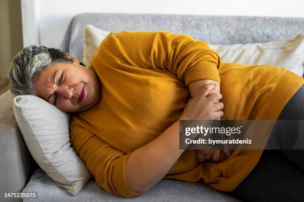 woman suffering from stomach cramps on the sofa at home - hernia recovery stock pictures, royalty-free photos & images