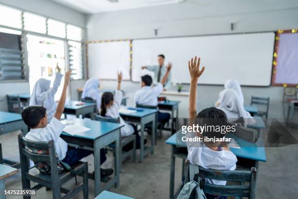 students raising their arms during teacher's lesson at elementary school - malaysia school stock pictures, royalty-free photos & images