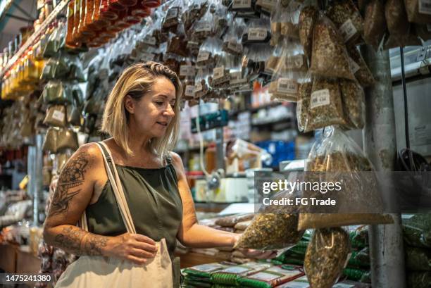mature woman looking at herbs in a spice store - bazar de especiarias imagens e fotografias de stock