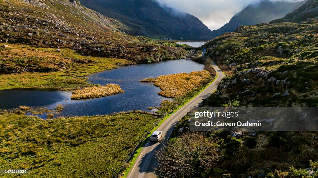 Gap of Dunloe, County Kerry, car driving on lakeside mountain road, aerial view of scenic mountain pass, aerial nature and road view, aerial view of winding road, nature relaxation video, car driving on winding road between mountains