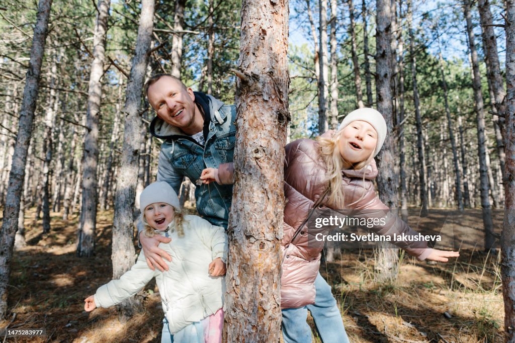 Cheerful family peeking out from behind a tree