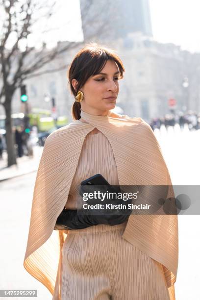 Carlotta Rubaltelli wears Issey Miyake trousers, top and cape with black leather gloves and gold earrings on March 03, 2023 in Paris, France.