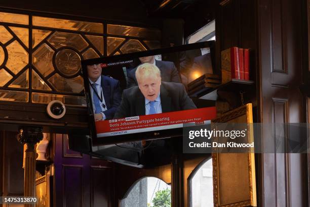People sit in the Red Lion pub as former Prime Minister Boris Johnson giving evidence on Partygate is shown on the TV on March 22, 2023 in London,...