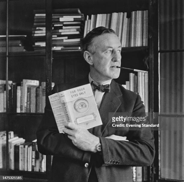 Author Ian Fleming smoking in his study while holding a book of new 'James Bond' short stories called 'For Your Eyes Only', April 4th, 1960.