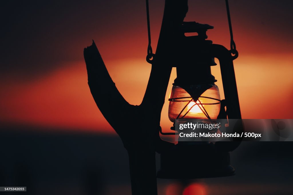 Close-up of silhouette of hand holding lantern against sky during sunset