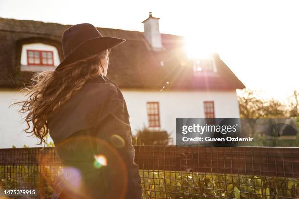 village house in old irish traditions, thatched cottage and young girl, irish girl and irish village house, traditional english house, back view of girl holding garden fence, thatched cottage irish village, british village house, irish village house - beautiful irish person stockfoto's en -beelden