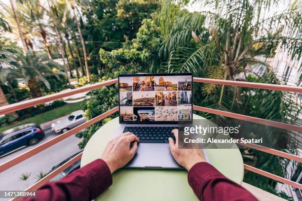 man working on laptop on a balcony surrounded by palm trees on a sunny day - person surrounded by computer screens stock-fotos und bilder