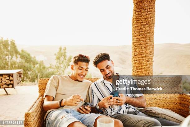 medium shot men looking at smart phones while relaxing at desert camp - middle eastern male on phone isolated stock pictures, royalty-free photos & images