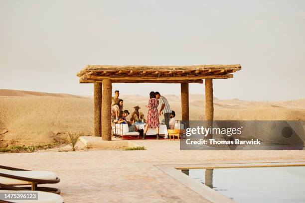 wide shot friends relaxing and sharing drinks at luxury desert camp - desert pool party stock pictures, royalty-free photos & images