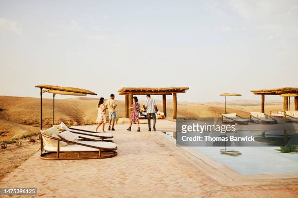 wide shot rear view of friends walking to party by pool at desert camp - desert pool party stock pictures, royalty-free photos & images