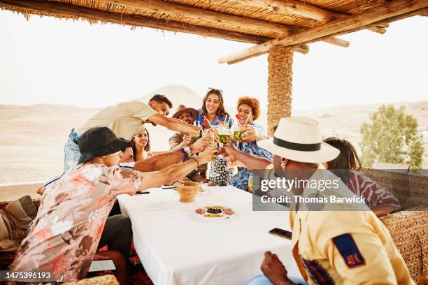 wide shot friends on vacation toasting drinks at luxury desert camp - toast around the world celebration stock pictures, royalty-free photos & images