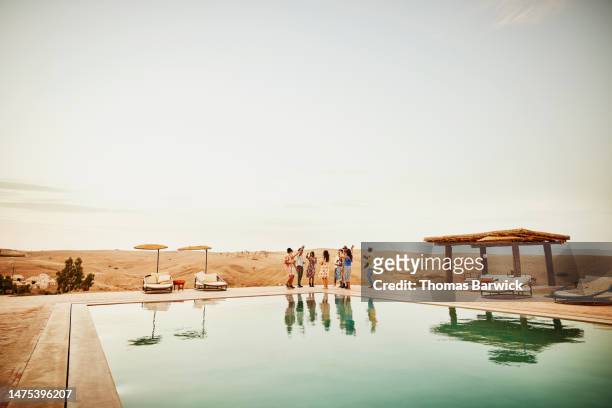 wide shot friends sharing drinks and dancing by pool at desert camp - desert pool party stock pictures, royalty-free photos & images