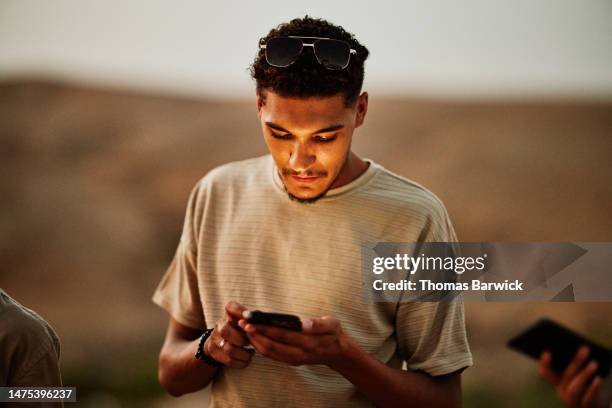 medium shot man looking at smart phone at desert camp at sunset - desertman stock pictures, royalty-free photos & images